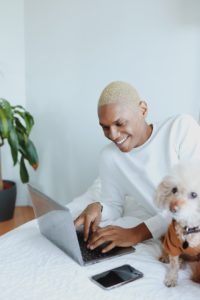 Person on bed with computer and dog
